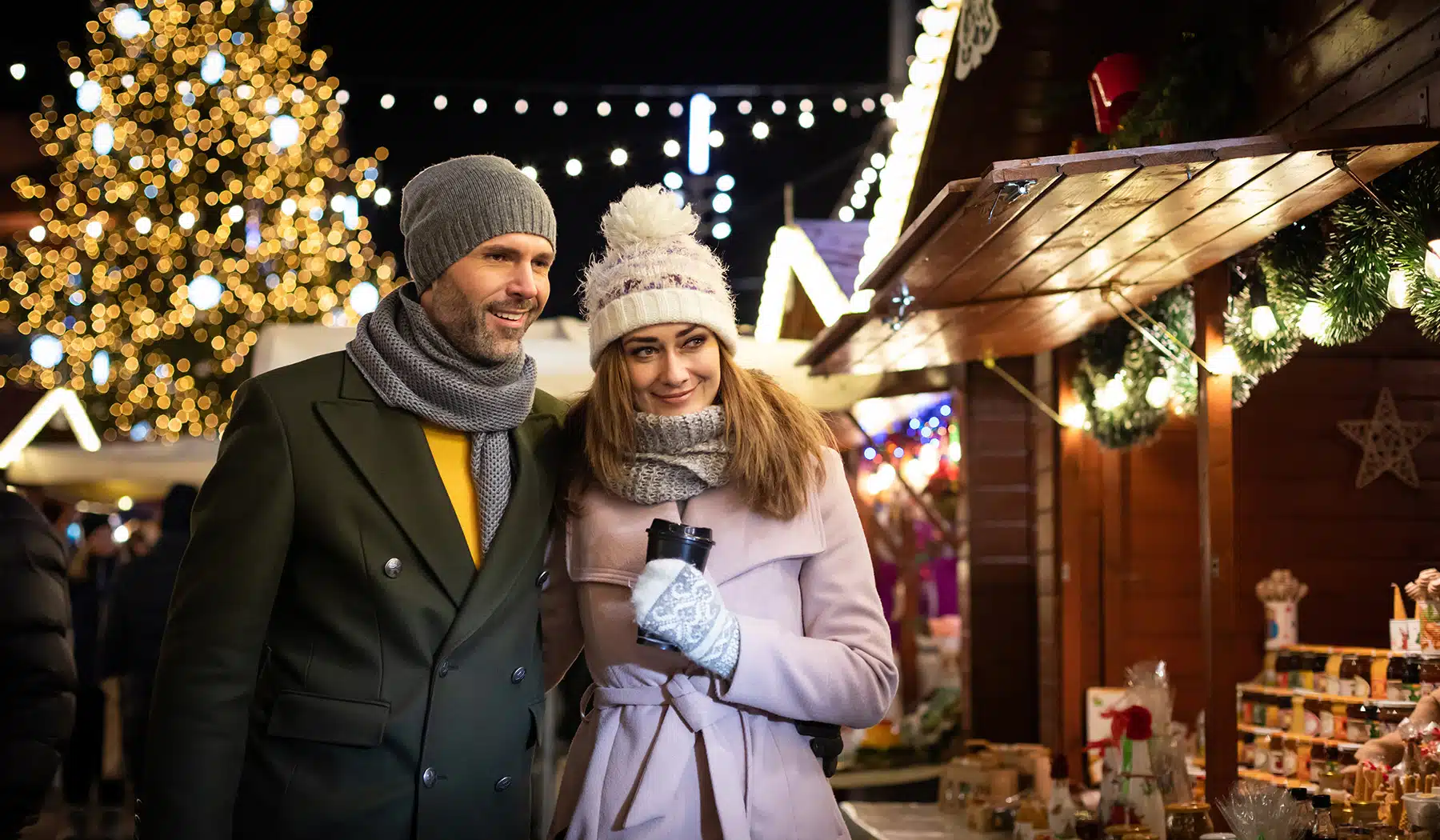 Loving couple visits the decorated Christmas market during the evening